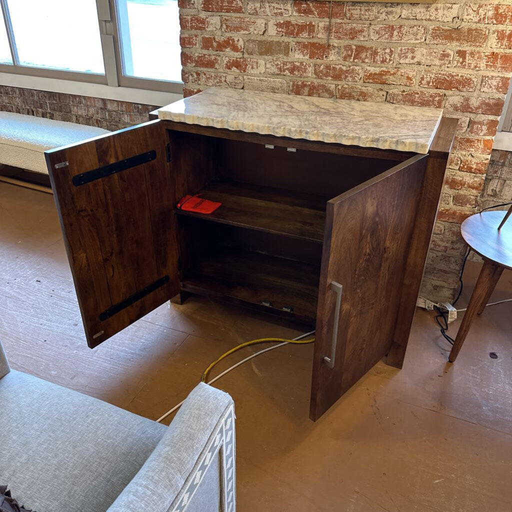 Wooden cabinet with open doors in a room with brick walls and a gray chair.