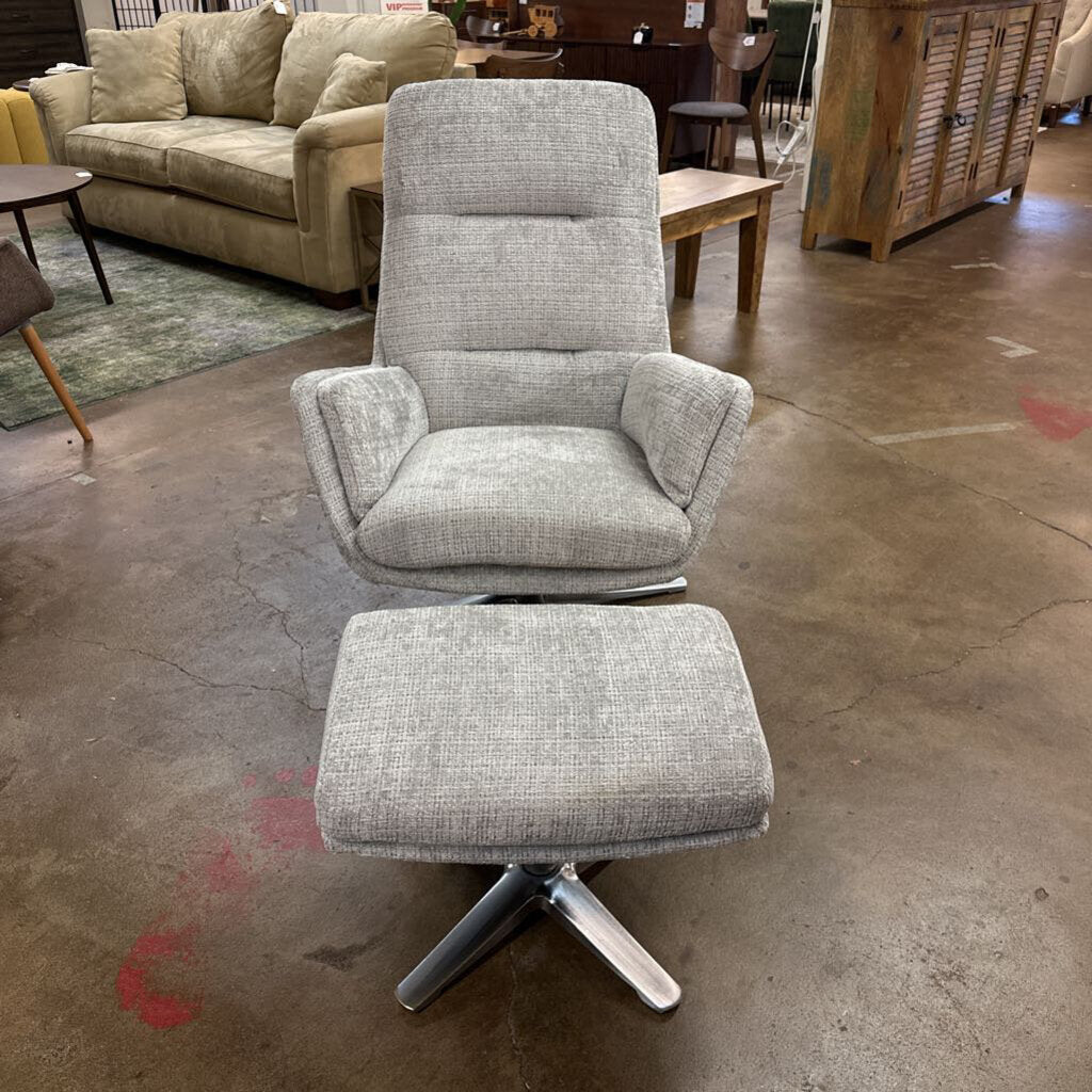 Gray upholstered chair with ottoman on a concrete floor in a furniture store.