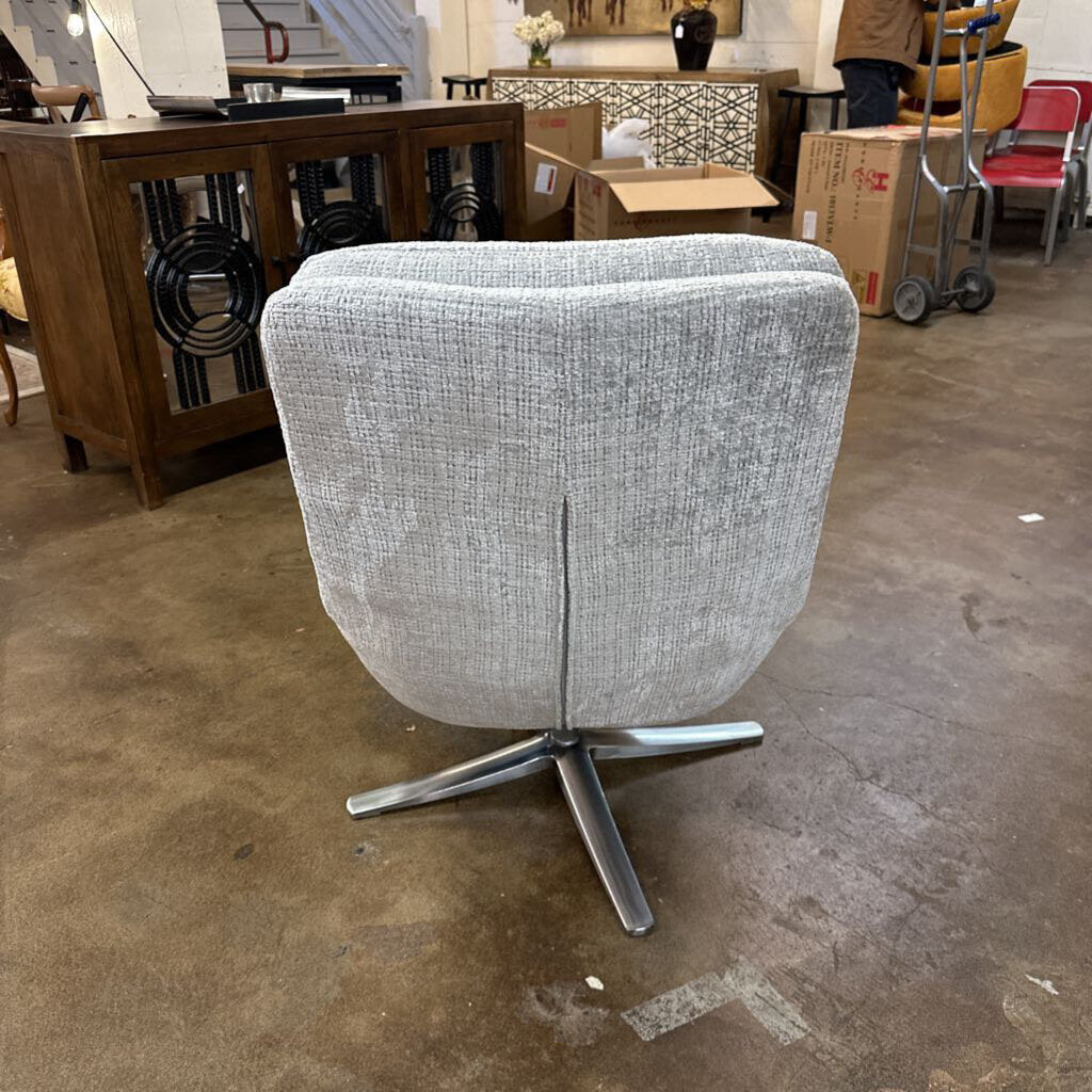 Gray swivel chair in a warehouse setting with boxes and furniture in the background