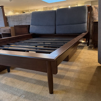 Wooden bed frame with blue upholstered headboard in a showroom setting
