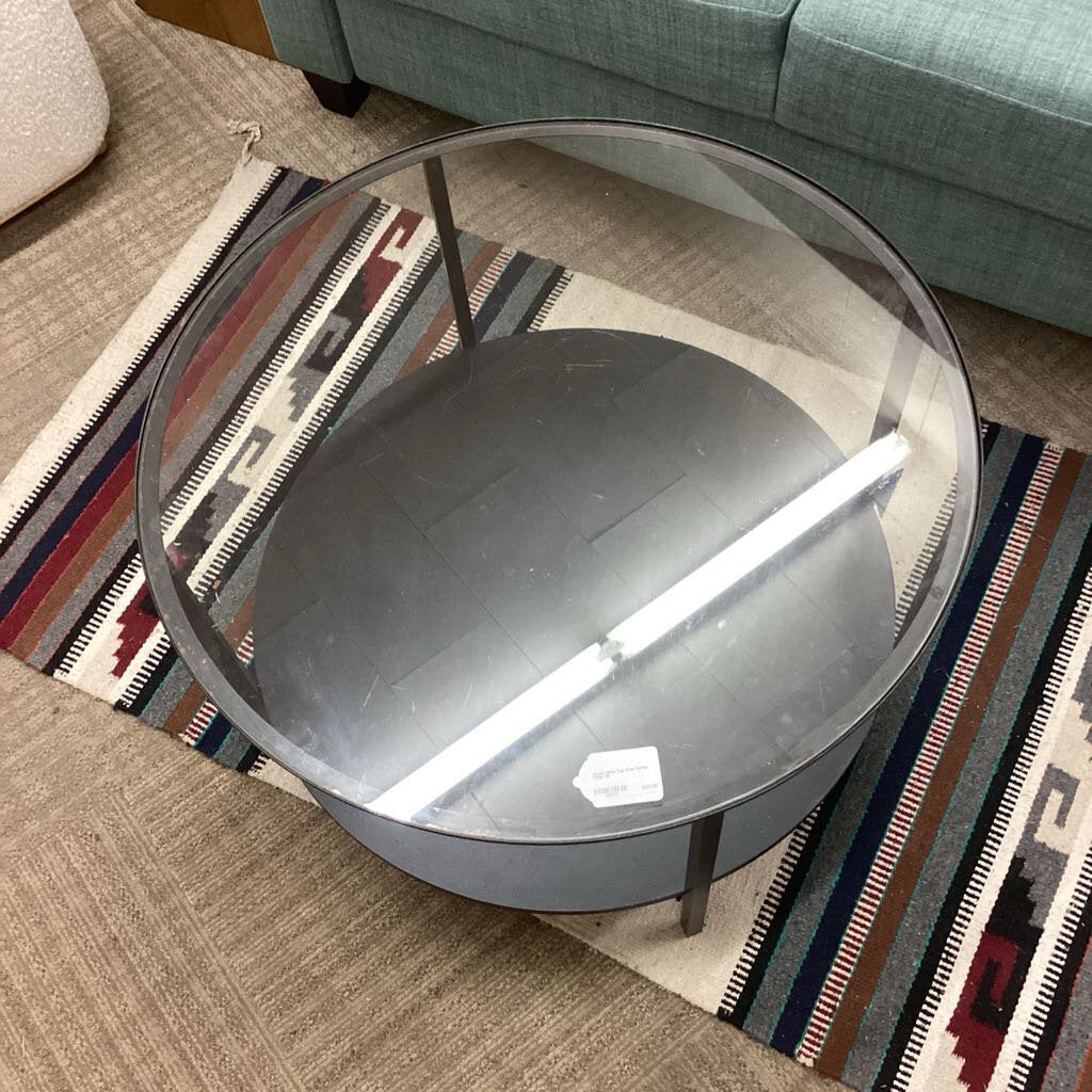 Round glass coffee table on a patterned rug with a couch in the background
