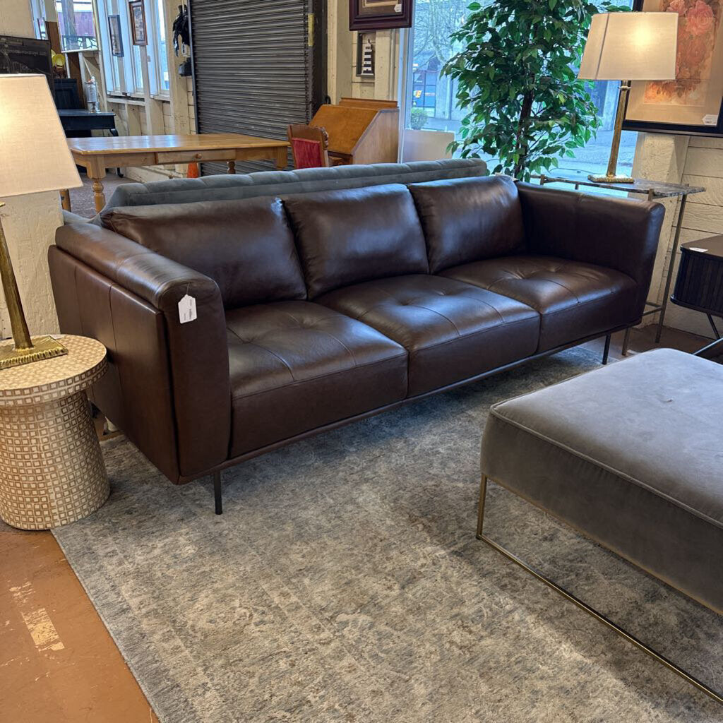 Brown leather sofa in a living room setting with a lamp and ottoman.