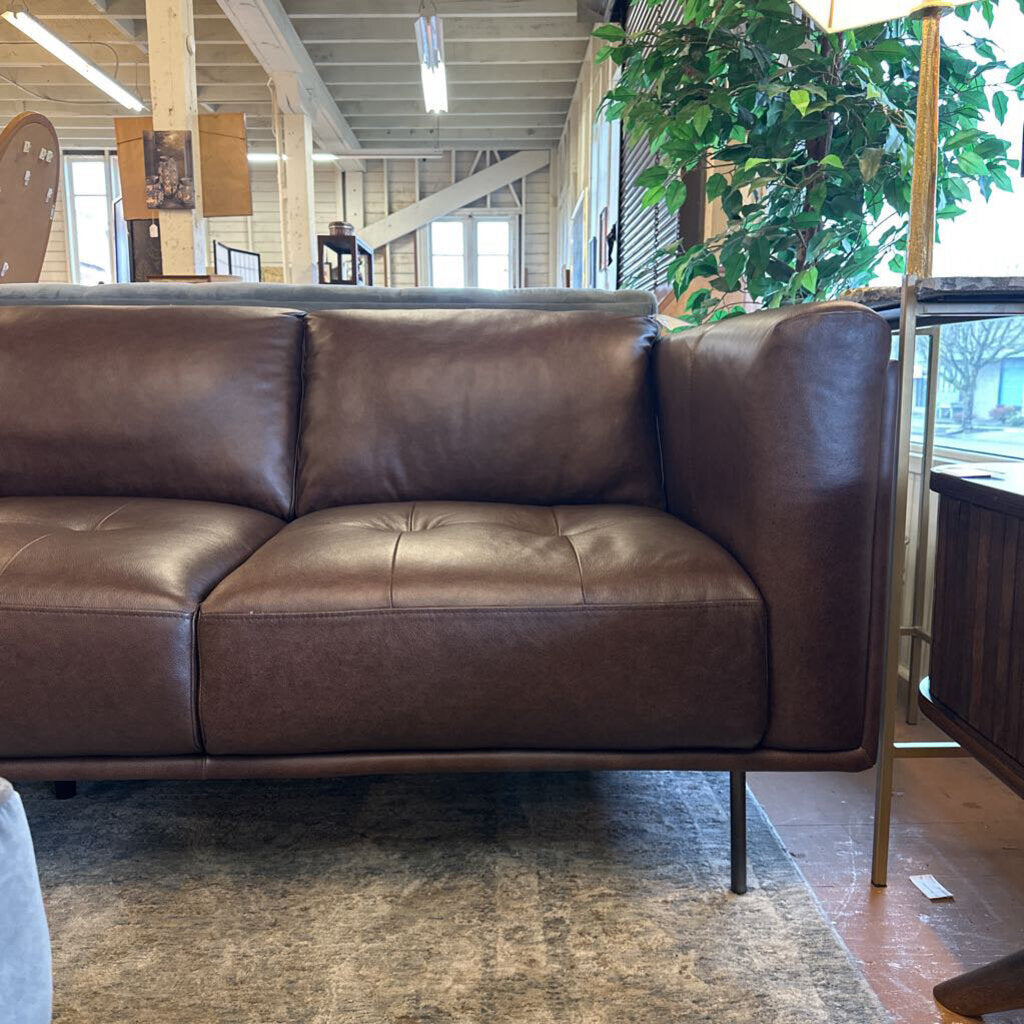 Brown leather sofa in a room with plants and a rug