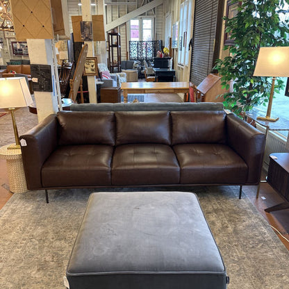 Brown leather sofa with ottoman in a room with tables and chairs
