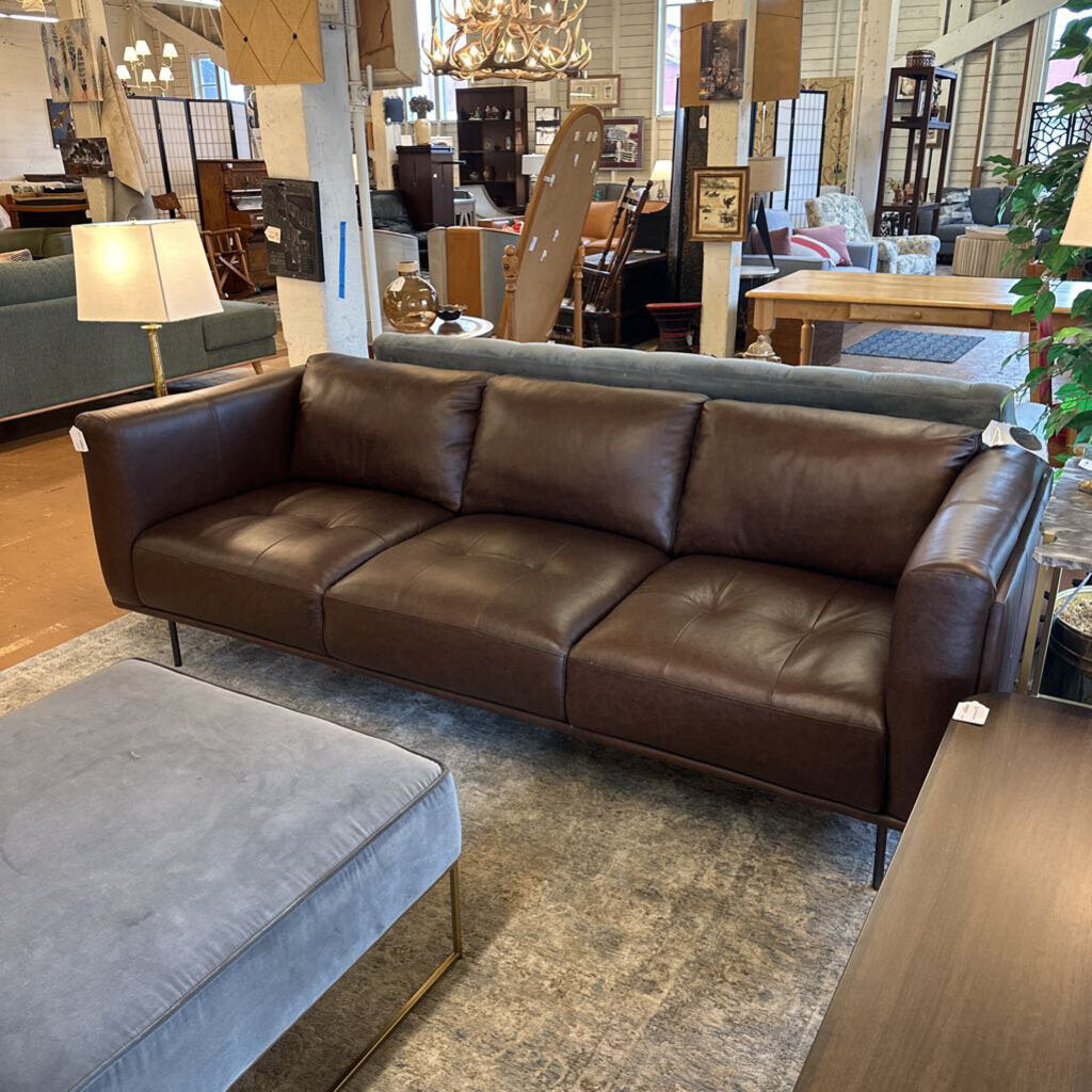 Brown leather sofa in a showroom setting with other furniture and decor.