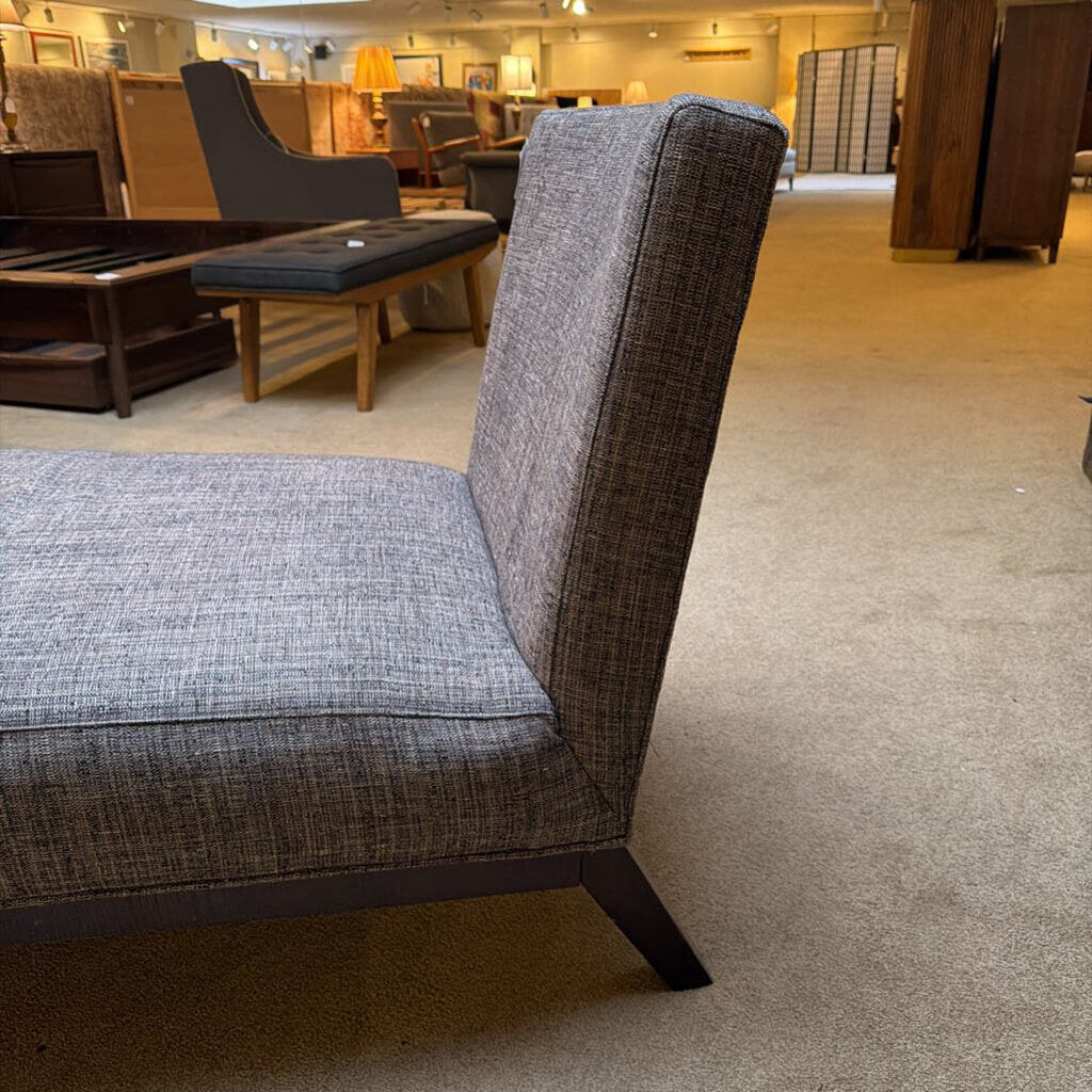 Gray upholstered chair in a showroom setting with other furniture in the background.