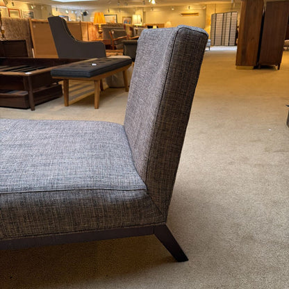 Gray upholstered chair in a showroom setting with other furniture in the background.