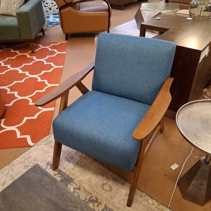 Blue armchair with wooden arms and legs in a room with a patterned rug and furniture.