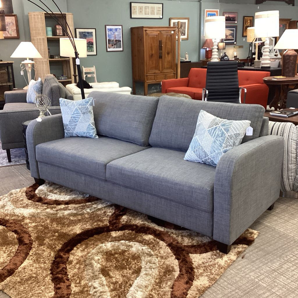 Gray sofa with decorative pillows on a patterned rug in a furniture store setting.