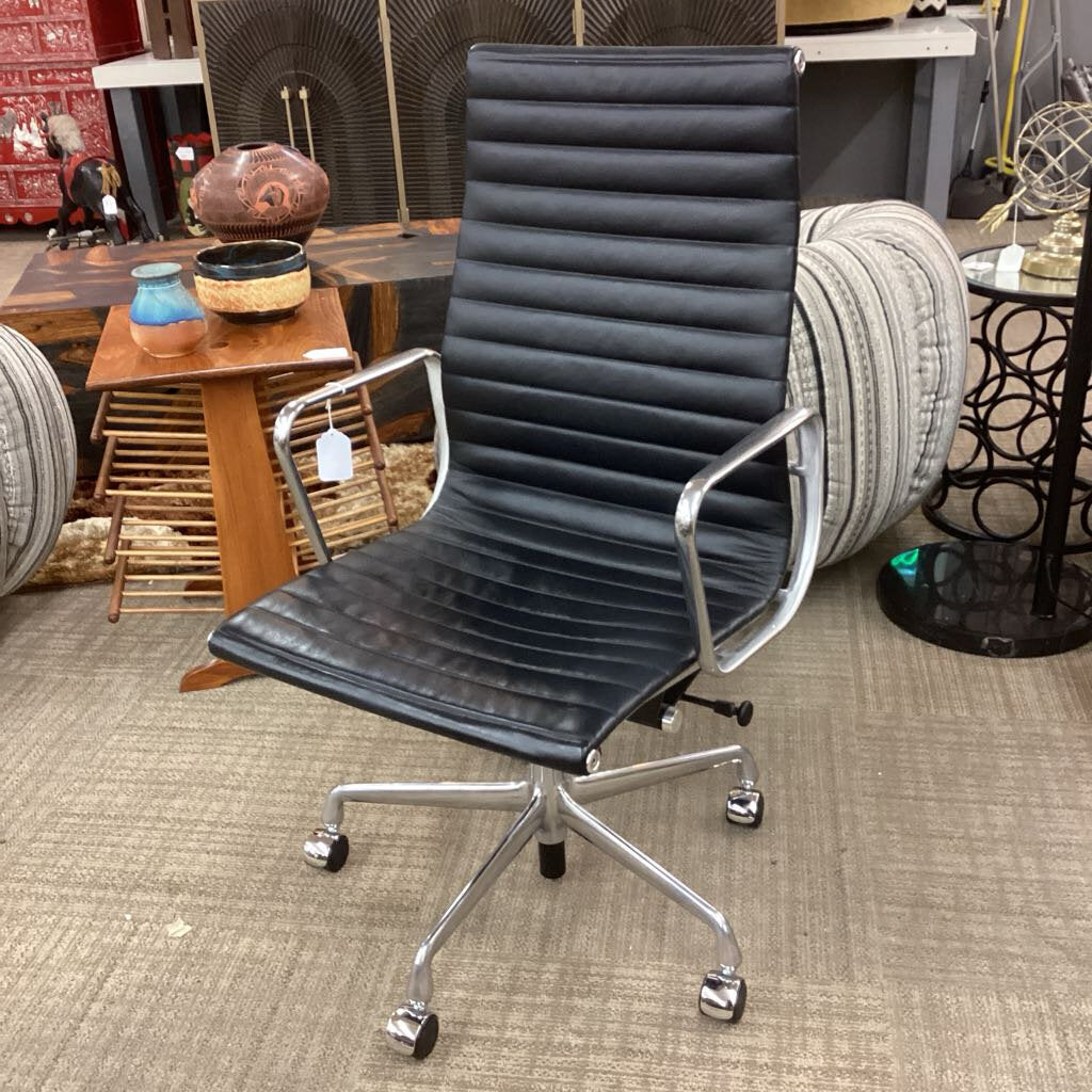 Black office chair with ribbed design in a room with various items on tables.