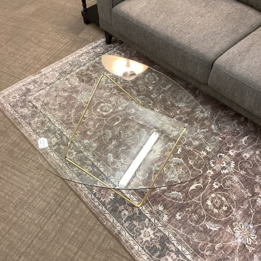 Glass coffee table with gold legs on a patterned rug in a living room setting.
