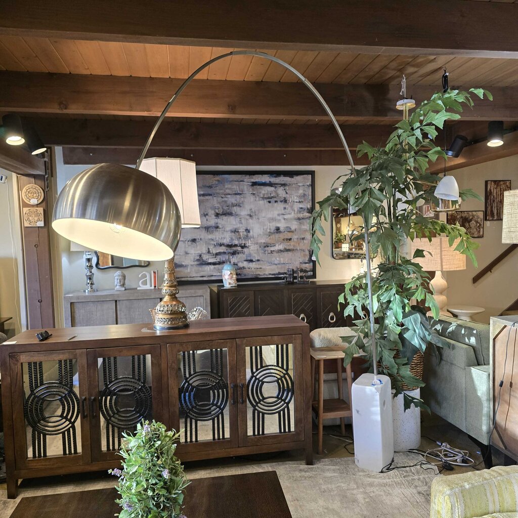 Living room with a large metallic floor lamp, wooden cabinet, and decorative plants.