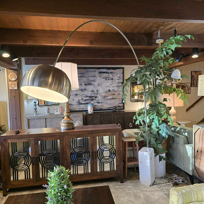 Living room with a large metallic floor lamp, wooden cabinet, and decorative plants.