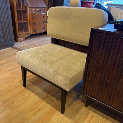 Beige armchair on a wooden floor with a wooden cabinet in the background