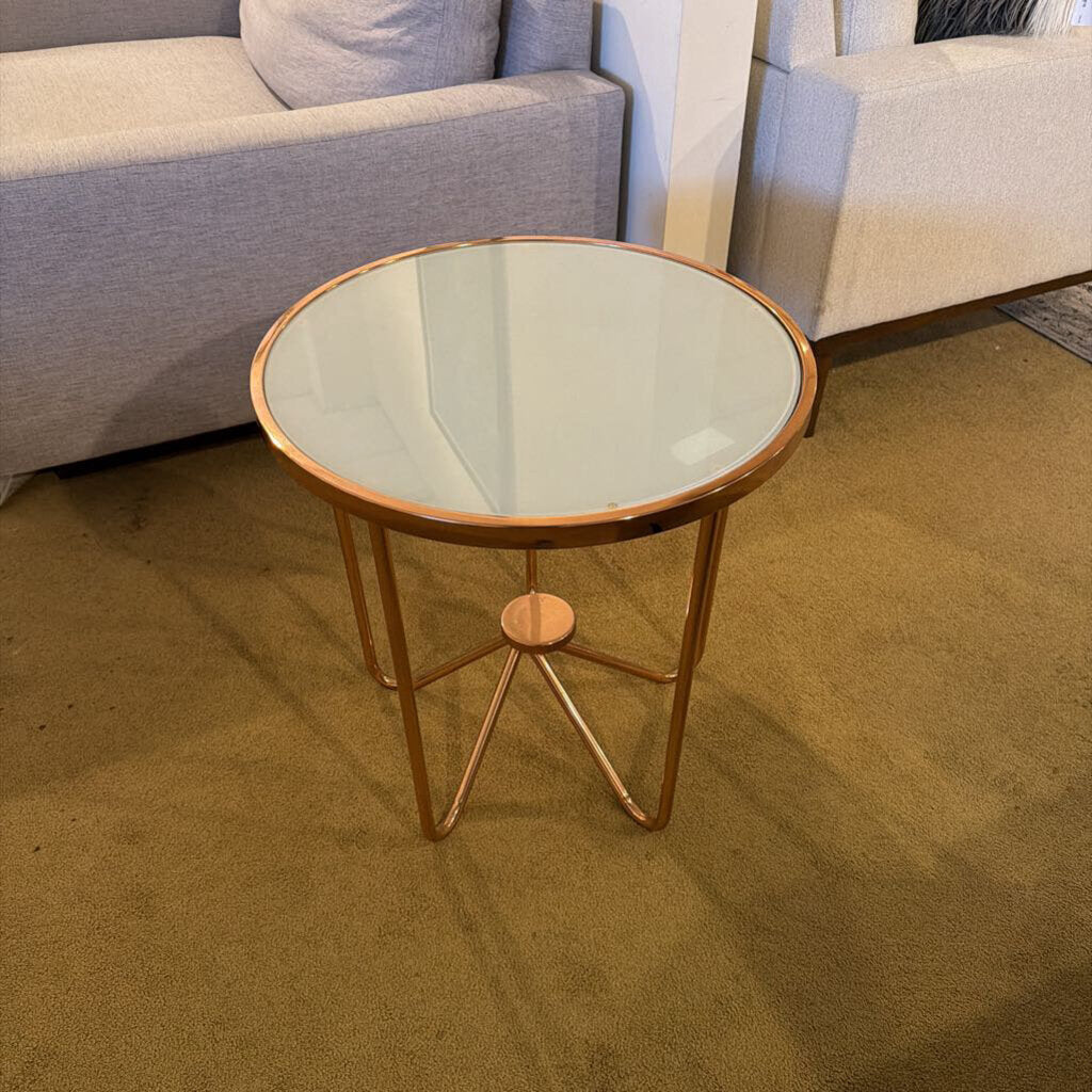 Round glass side table with gold metal legs in a living room setting