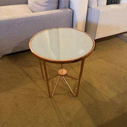 Round glass side table with gold metal legs in a living room setting