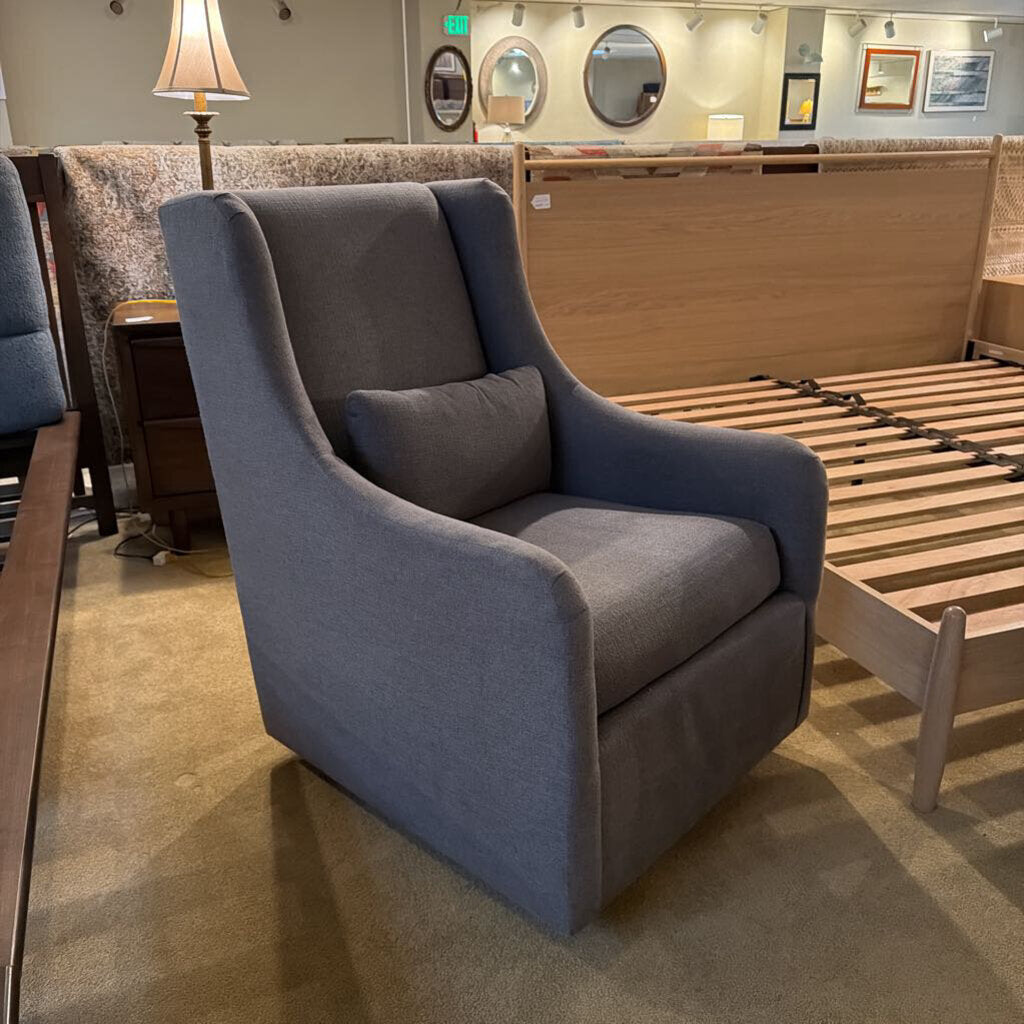 Gray upholstered chair in a showroom setting with wooden furniture and mirrors in the background.