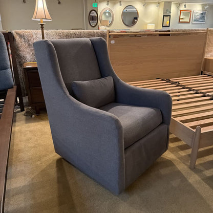 Gray upholstered chair in a showroom setting with wooden furniture and mirrors in the background.