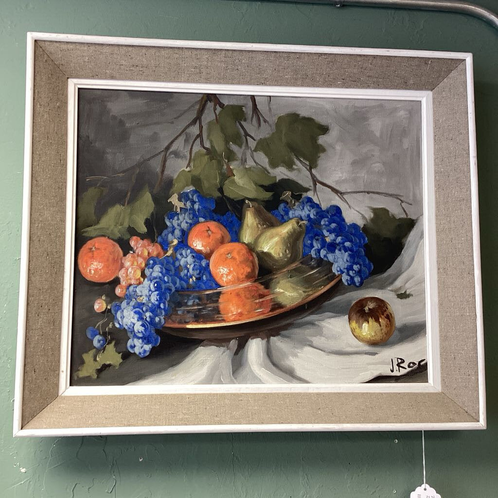 Framed still life painting of fruits and blue flowers on a light green wall.