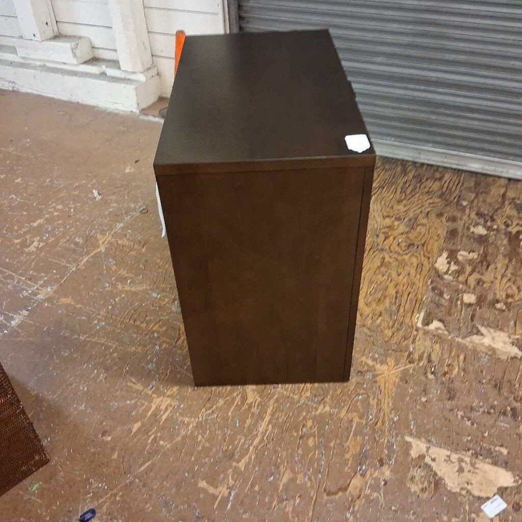 Dark brown cube-shaped object on a wooden floor with a metal shutter in the background