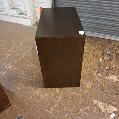 Dark brown cube-shaped object on a wooden floor with a metal shutter in the background