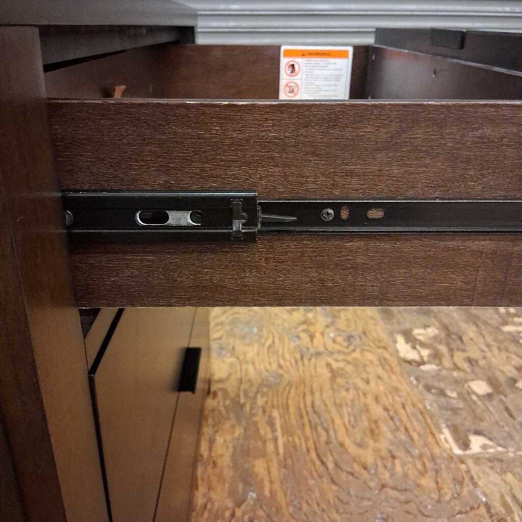 Wooden drawer with a metal handle and warning label on a wooden floor.