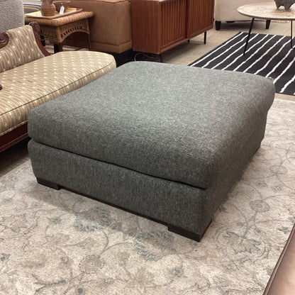 Gray ottoman in a living room setting with furniture and decor.