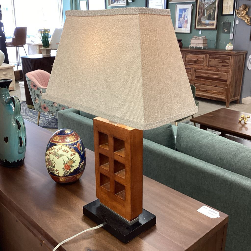 Table lamp with wooden base and beige shade on a wooden table in a room setting.