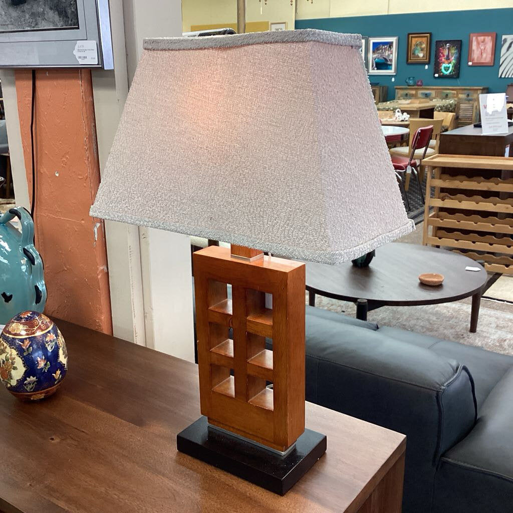 Table lamp with wooden base and gray shade on a table in a room setting.