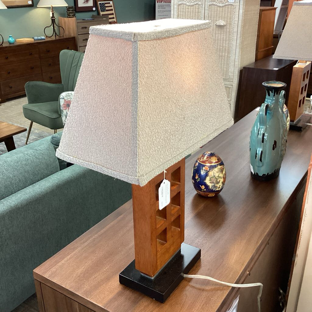 Table lamp with a textured white shade on a wooden table in a room setting.