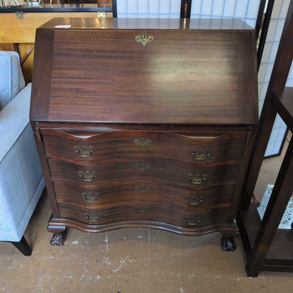 Wooden dresser with curved design and brass handles on a wooden floor.