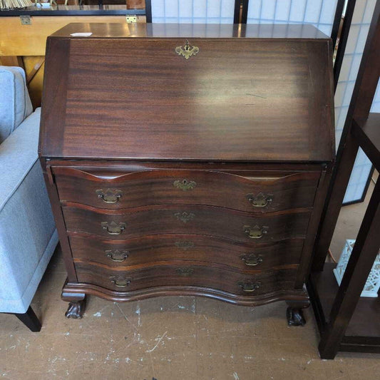 Wooden dresser with curved design and brass handles on a wooden floor.