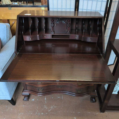 Wooden desk with multiple drawers and a shelf in a room setting.