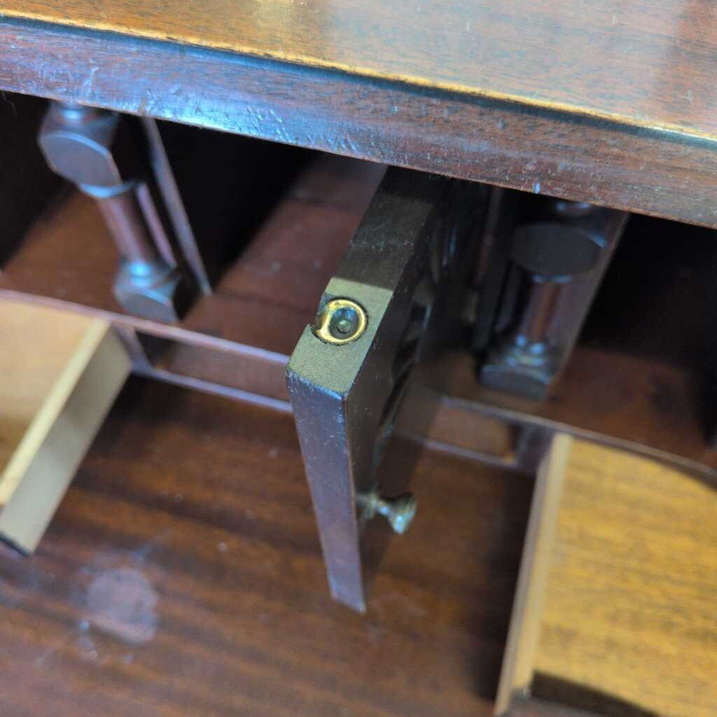 Close-up of a wooden desk with metal legs and a small round object on one of the legs.