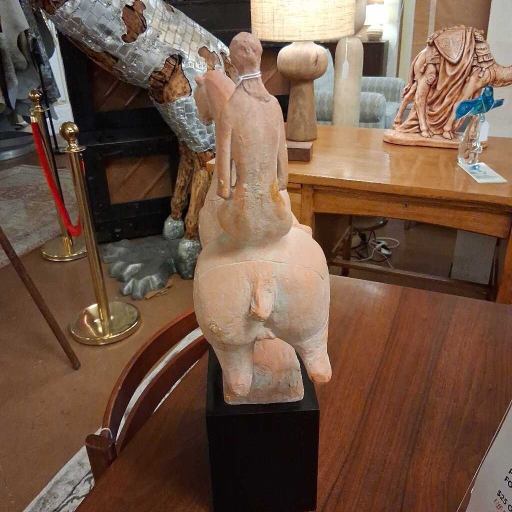 Decorative sculpture on a pedestal in an indoor setting with other sculptures and furniture.