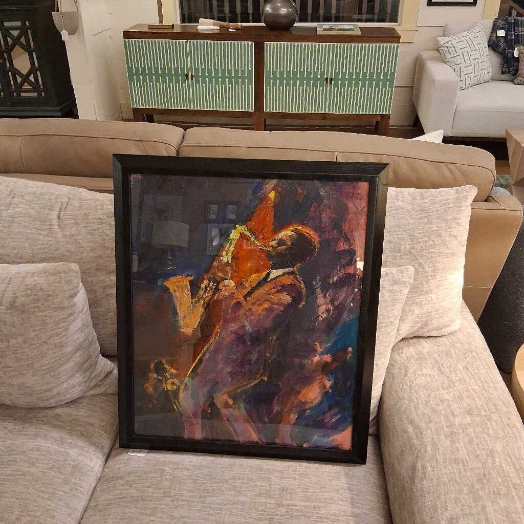 Framed abstract painting on a couch with a decorative cabinet in the background