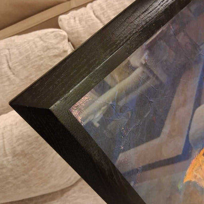 Close-up of a framed painting with a dark wood frame on a textured surface.