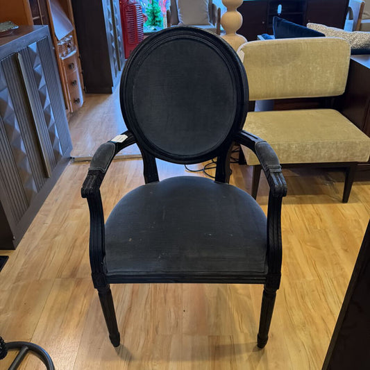 Black armchair on a wooden floor with other furniture in the background