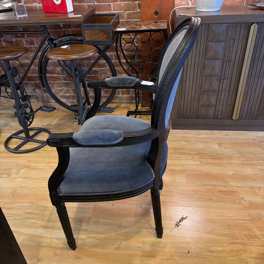 Chair with wooden armrests and cushioned seat in a room with wooden floor and brick wall.