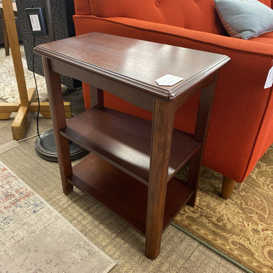 Wooden side table with two shelves next to an orange sofa on a patterned rug.