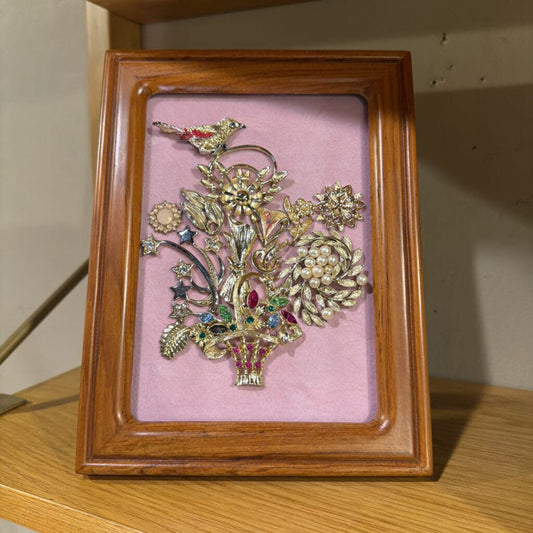 Decorative brooch in a wooden frame on a pink background