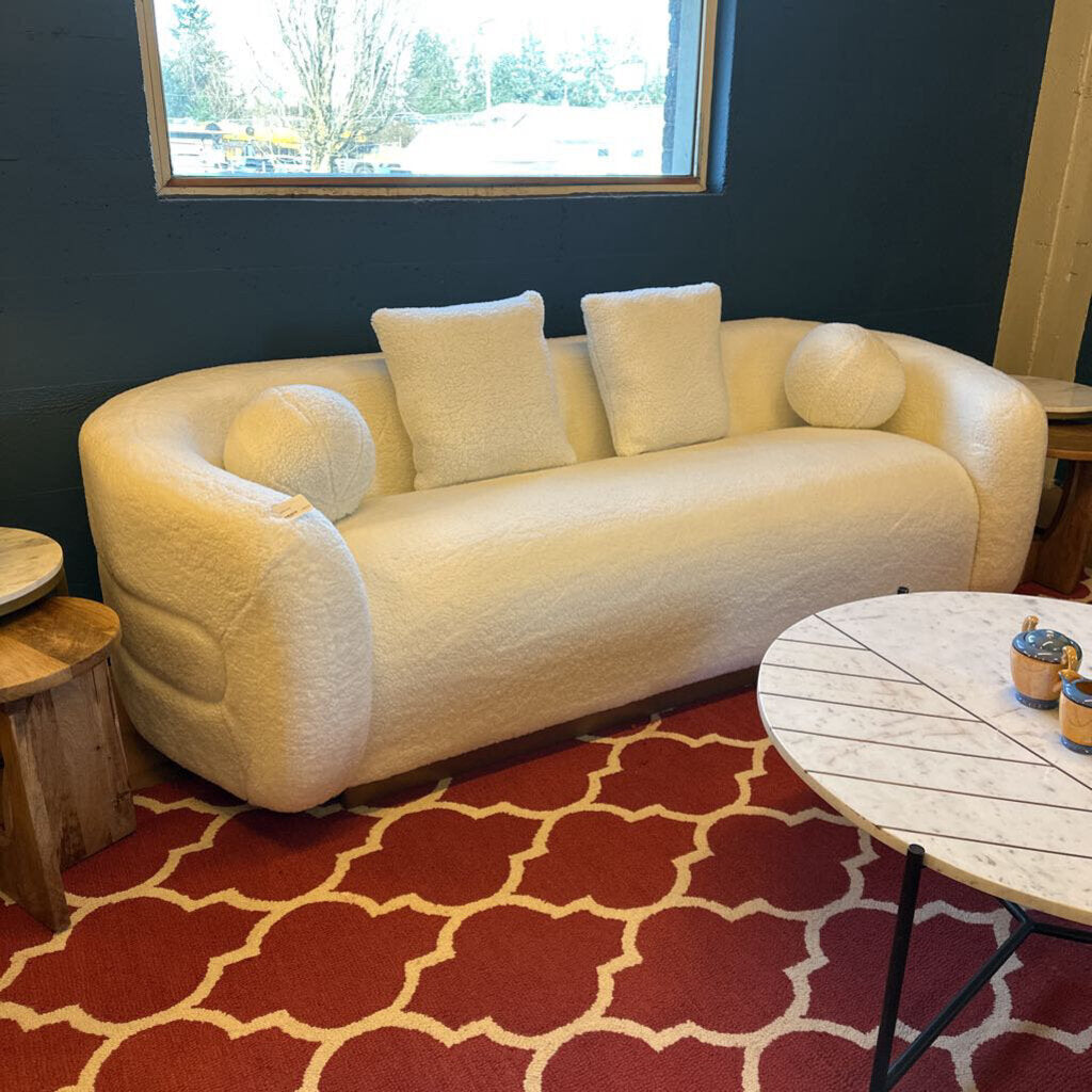 Beige sofa in a room with a red and white patterned rug and a window in the background.