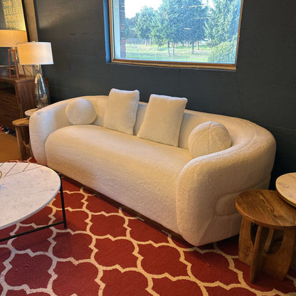 White sofa with cushions on a red patterned rug in a room with a window and furniture.