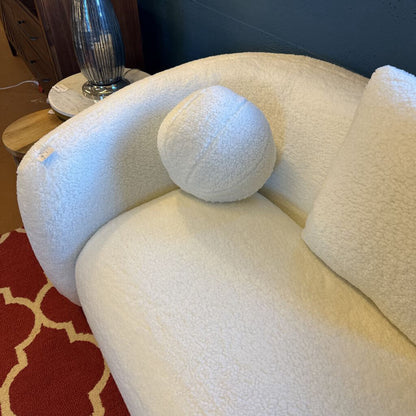 White textured sofa with a round cushion on a red patterned rug
