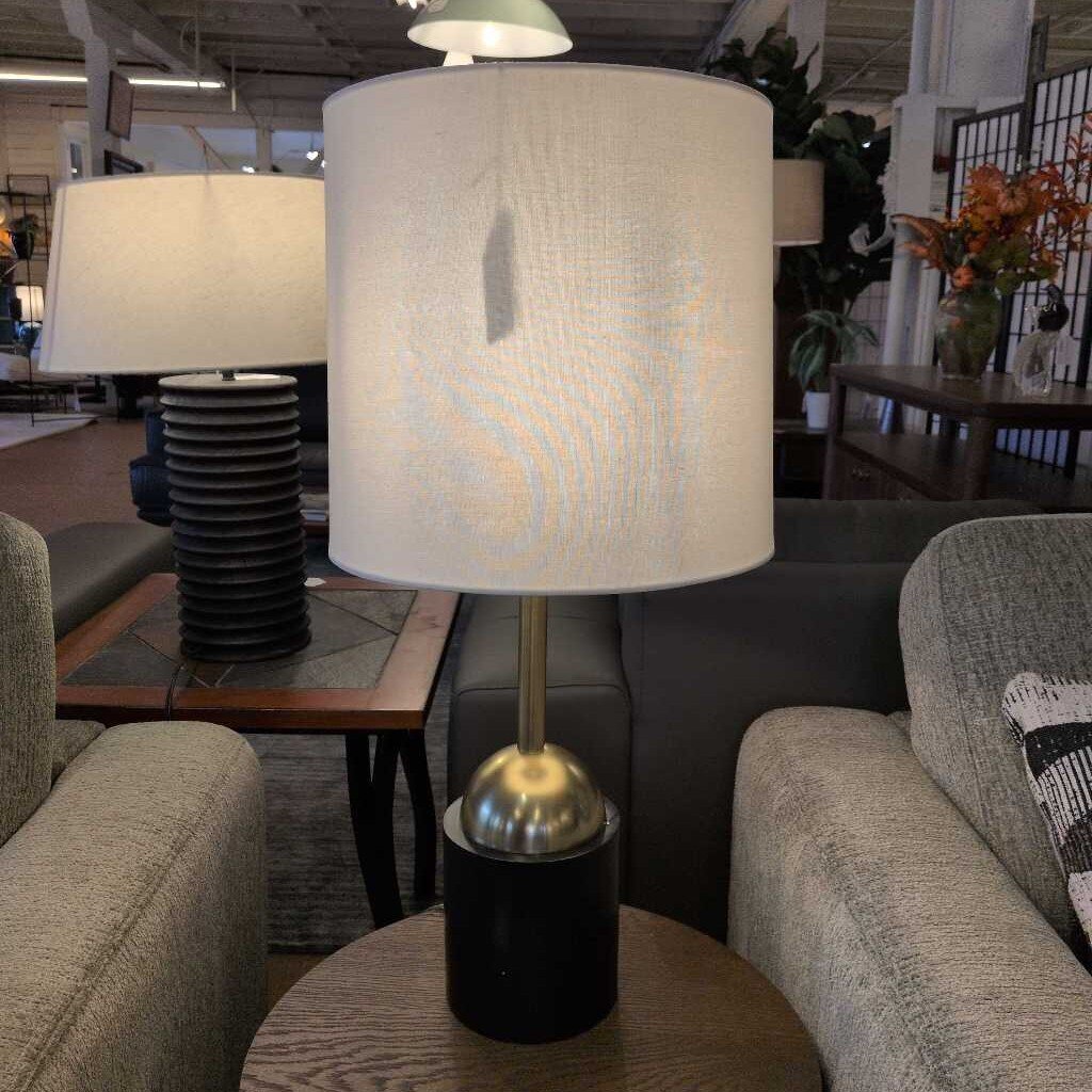 Table lamp with a white textured shade on a wooden table in a furniture store.