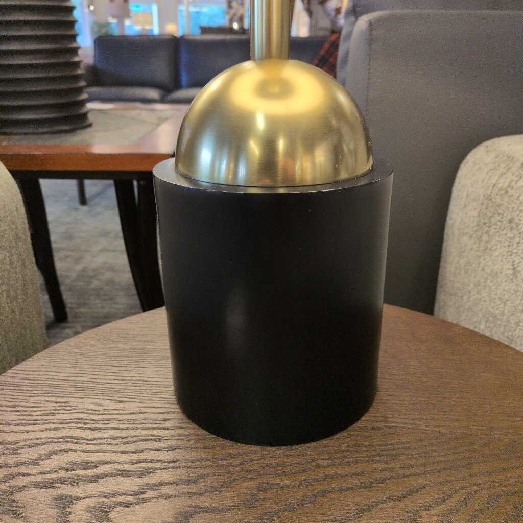Black cylindrical container with gold lid on a wooden table