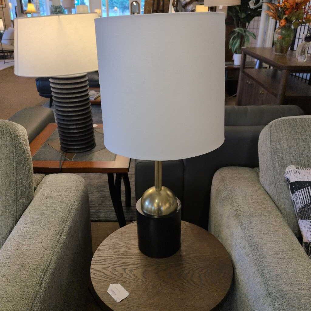Table lamp with white shade and black base on a wooden table in a living room setting.