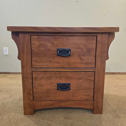 Wooden nightstand with two drawers on a carpeted floor.