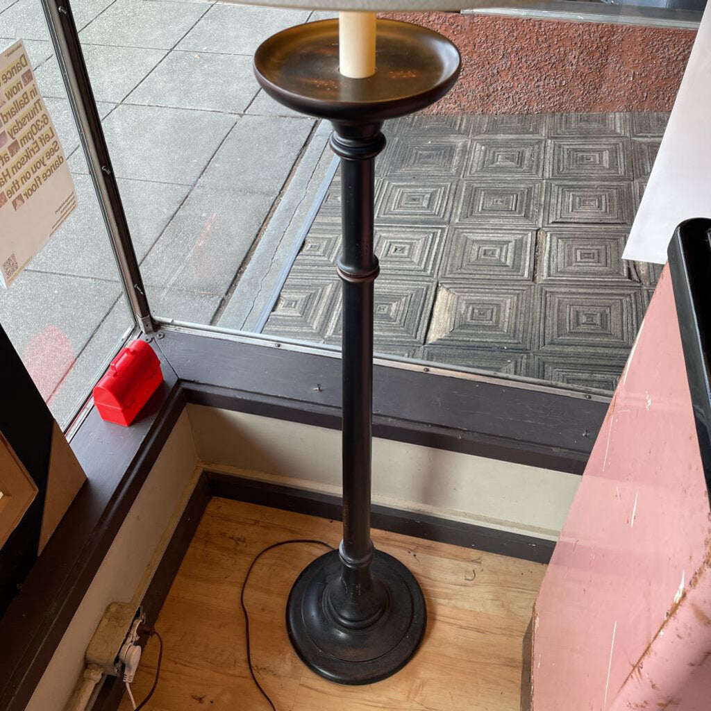 Black candle holder with a white candle on a wooden floor next to a glass door.