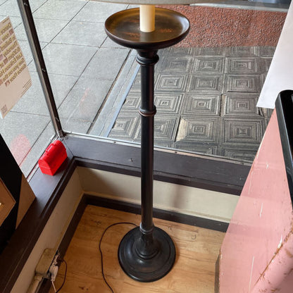 Black candle holder with a white candle on a wooden floor next to a glass door.